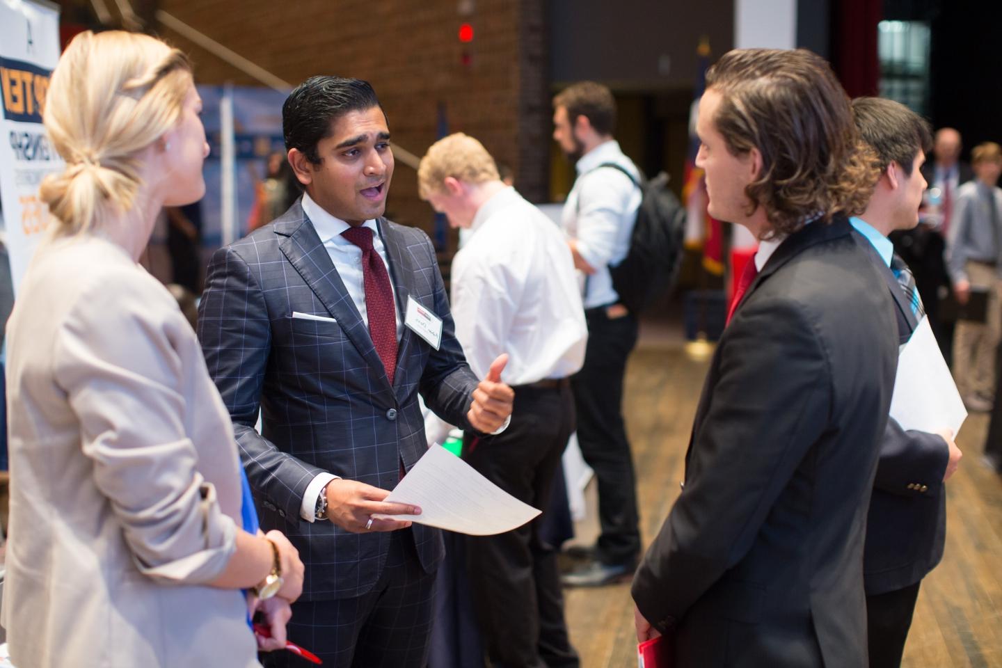 a student in a suit speaks with two potential employers in Laurie Auditorium at a Career Fair